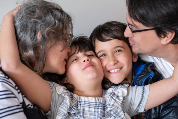 A joyful family of four sharing a warm embrace, highlighting love and togetherness indoors.