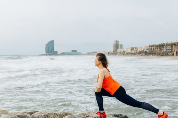 A woman stretches by the ocean in Barcelona, showcasing health and fitness by the sea.